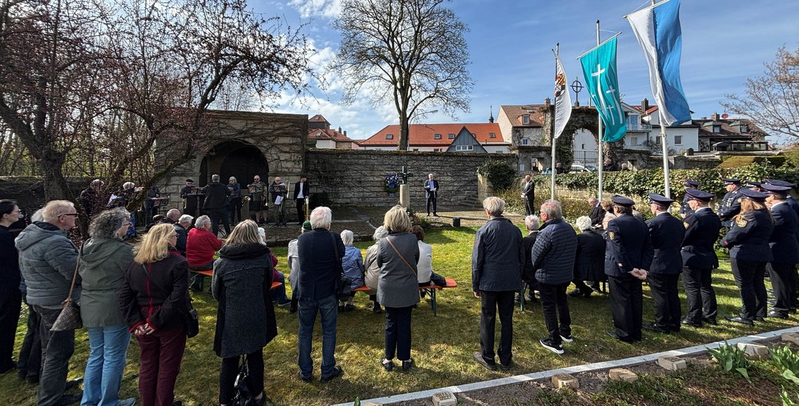 Menschen stehen und sitzen andächtig auf einem Friedhof.