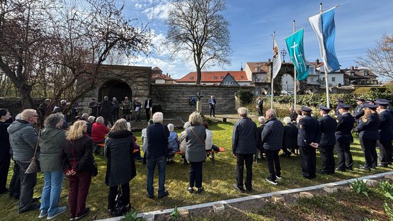 Menschen stehen und sitzen andächtig auf einem Friedhof.